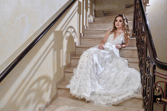 Beautiful girl in fashion dress posing on front staircase. Fashion portrait of a beautiful woman in white dress. Romantic image.