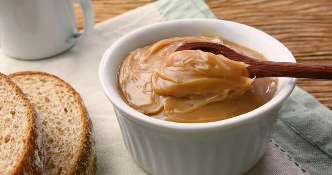 Hand getting doce de leite, traditional brazilian creamy milk sweet with bread and coffee over wooden table