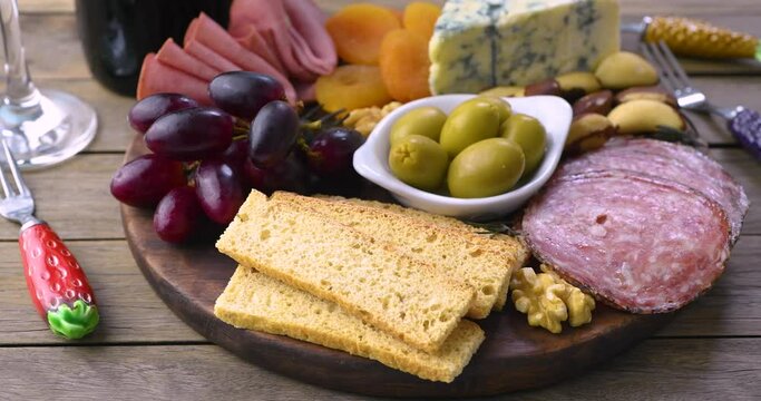 Appetizer board with cheese, nuts, fruits, toasts, wine and charcuterie over wooden table