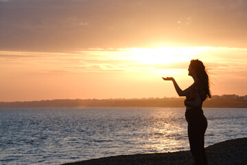 Fototapeta premium silhouette of a woman on the beach holding the sunset