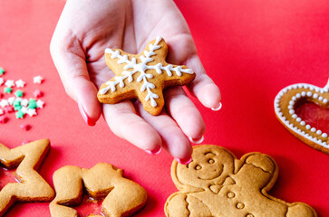 Christmas gingerbread with sugar icing on a female hand on a red background