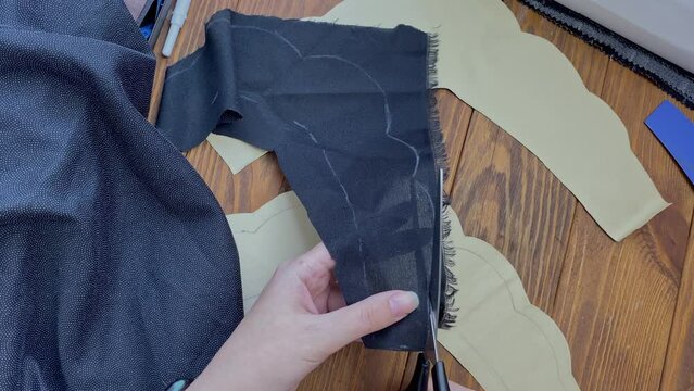 Women's hands cut out a piece of an ethnic Slavic crown on a wooden table with scissors from an adhesive woven interlining fabric. Seamstress and her workplace. Hobby and handicraft.
