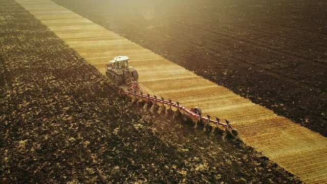 Tractor with harrow system plowing ground on cultivated farm field, preparing soil for planting new crop, agriculture concept, top view