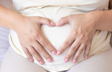 pregnant woman holding heart shape with both hands from fingers over big belly.bright light photo...