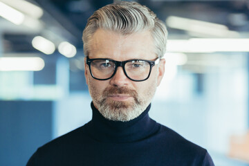 Fototapeta premium Close-up photo portrait of successful serious and mature businessman, investor in glasses looking thoughtfully at camera, man at work inside office