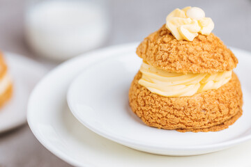 Craquelin Choux biscuits with cream vanilla filling pored with chocolate on light grey background. Traditional french pastry and dessert