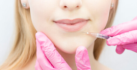A woman with beautiful clear skin. A cosmetologist makes injections to increase the lips and anti-wrinkles of a beautiful woman. Women's cosmetology in a beauty salon.