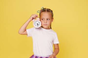 Portrait of a cute girl with a small alarm clock on a yellow background