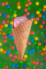 Pink ice Ccream ball in waffle corn on green background with round colorful chocolate buttons