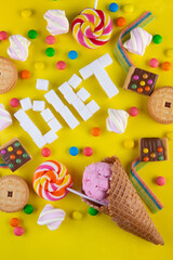 Fototapeta na wymiar colorful array of different childs sweets and treats on yellow background. Candies with jelly, chocolate, ice cream, lollipops, cookie, marshmallow and title DIET, white sugar cubes Top view, flat lay