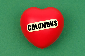On a green surface lies a red heart with the inscription - Columbus