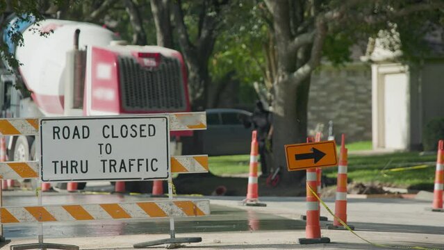 Focus on a road closed sign with a cement truck in the background during resurfacing of a neighborhood street.