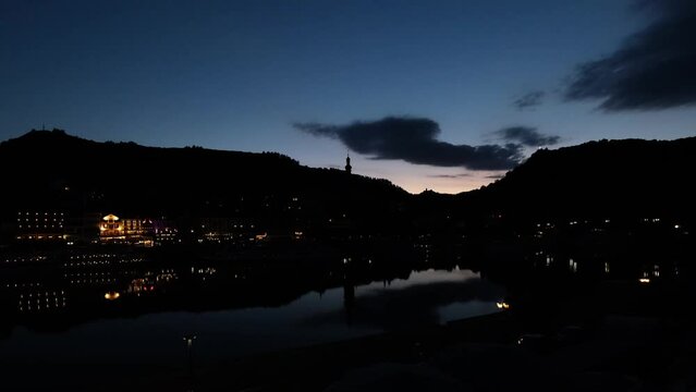 Cochem, the romantic medieval town and the River Moselle by night. Historical German city in blue hour with evening lights. Partly cloudy colourful sky and beautiful water reflections after sunset. 4K