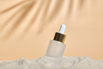 face serum of glass bottle with a pipette on a natural background with sand. Essential oil for...