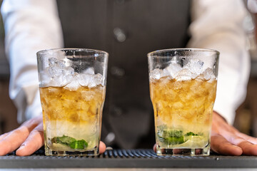 Barman serves Mojito in night club adding ingredients and creating expert drinks on bar counter.