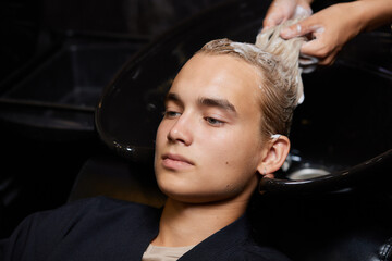Fototapeta na wymiar Hairstylist Hairdresser Washing Customer Hair - Young Man Relaxing In Hairdressing Beauty Salon.