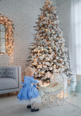 Baby girl wearing cute dress and headband, carries stroller in festively decorated room with garland of lights.