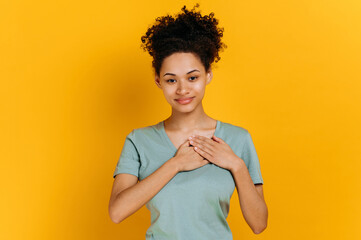 Pretty, candid african american smiling curly young woman with hands on heart and grateful gesture,...