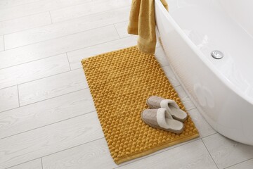 Soft orange bath mat and slippers on floor in bathroom