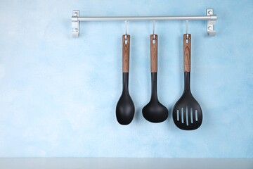 Rack with kitchen utensils hanging on light blue wall