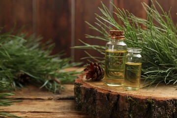 Pine essential oil, cone and branches on wooden table. Space for text