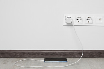 Modern smartphone charging from electric socket indoors. Space for text