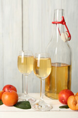 Delicious plum liquor and ripe fruits on white wooden table. Homemade strong alcoholic beverage