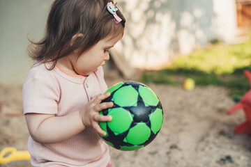 Baby girl portrait holding toy soccer ball and ready to throw it. Baby development. Active kid...