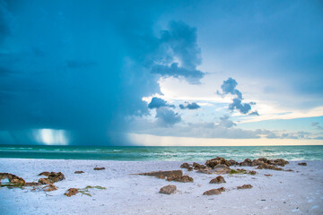 Siesta Key, Florida, popular travel tourist destination. Scene of the beach near Siesta Key Village at dusk as a storm appears in the distant sky. Cool blue turquois water along the rock studded shore