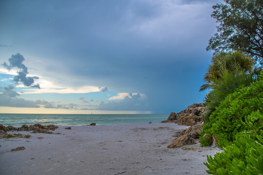 Siesta Key, Florida, popular travel tourist destination. Scene of the beach near Siesta Key Village at dusk as a storm appears in the distant sky. Cool blue turquois water along the rock studded shore
