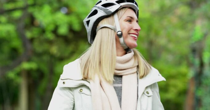 Happy, carefree woman riding a bicycle outdoors in a nature park as she lives an active and healthy lifestyle. Beautiful blonde female wearing a bike helmet enjoying her fun cycling hobby