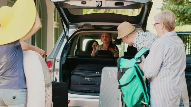 Casual family putting voyage trolleys in car trunk while getting ready for holiday vacation departure. People loading baggage and backpacks inside vehicle while going on summer citybreak together.