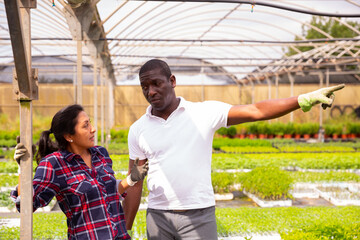 Portrait of dissatisfied african american farmer talking to latin workwoman in greenhouse