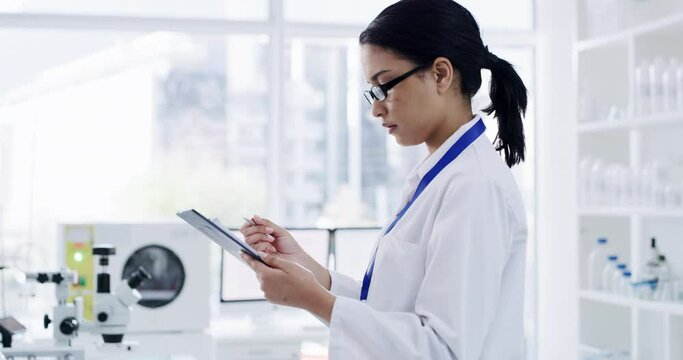 Serious female scientist working and writing patient information in a lab. Laboratory worker looking at and analyzing health data for a science journal. Medical professional doing a clinical trial