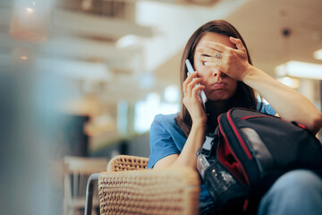 Unhappy Woman Talking on the Phone Waiting in an Airport. Stressed traveler speaking on her cellphone feeling overwhelmed
