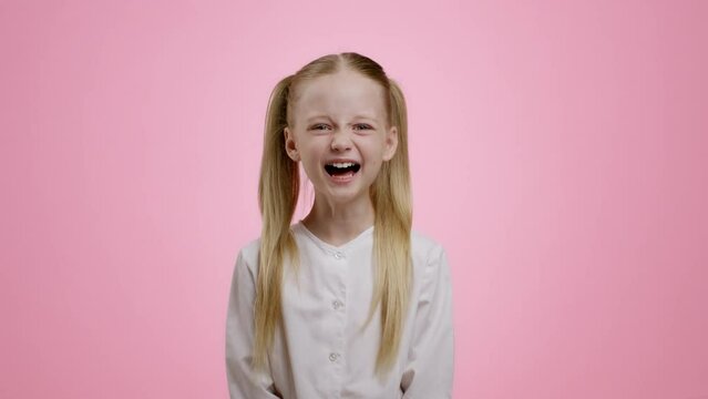 Sincere kid happiness. Adorable little girl with two ponytails laughing loud, pink studio background