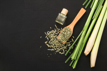 Fresh lemongrass with slices dry leaf in wooden spoon and lemon grass oil on black background , top view , flat lay.