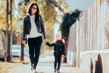 Mother and Little Daughter Walking Together Wearing Leather Jackets. Cool mom and girl matching their autumn outfits holding hands
