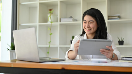 Successful Asian businesswoman using digital tablet and laptop computer