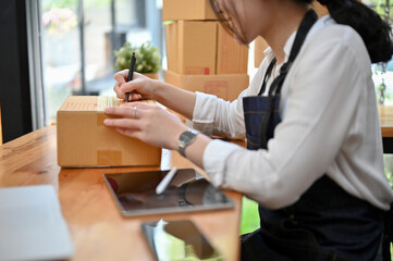 Pretty Asian female e-commerce startup preparing, writing a customer's address on a cardboard box.