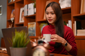 Attractive Asian businesswoman is sipping coffee while working on her laptop computer.