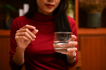 Attractive Asian female holding a glass of water and a tablet medicine. cropped image