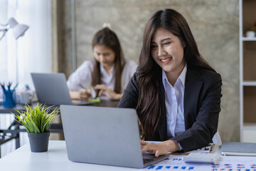 Two Asian women with laptop and financial graphs calculating accounting and taxes at the office. business idea