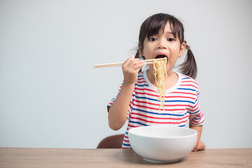 Cute Asian child girl eating delicious instant noodles at home.
