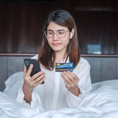 woman using mobile smart phone and credit card for online shopping while making order on bed in morning at home. technology, ecommerce, digital banking online payment and apartment living concept
