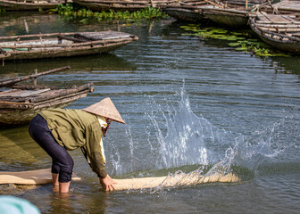 Unidentified woman washing a trational sedge mat on a lagoo.
