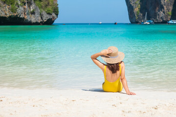 Woman tourist in yellow swimsuit and hat, happy traveller sunbathing at Maya Bay beach on Phi Phi...