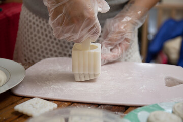 Making Mooncake. A mooncake is being moulded using plastic mould. The mould is being lifted, leaving the moulded mooncake on the board.