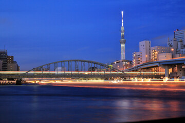 隅田川を通る鉄橋と屋形船の光跡と東京スカイツリーの夜景