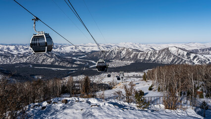 Cable car cabins on ropes over a snow-covered valley. A picturesque mountain range against the...
